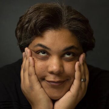 A photograph of Roxanne Gay with her face cupped in her hands whilst she rolls her eyes