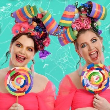 A photo of Sugarcoated Sisters wearing matching pink dresses and holding colourful lollipops