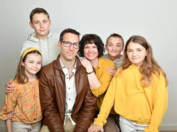 A studio photograph of The Marsh Family they parents are sat down and the children are stood around them, they are all wearing cream, brown and yellow and smiling at the camera